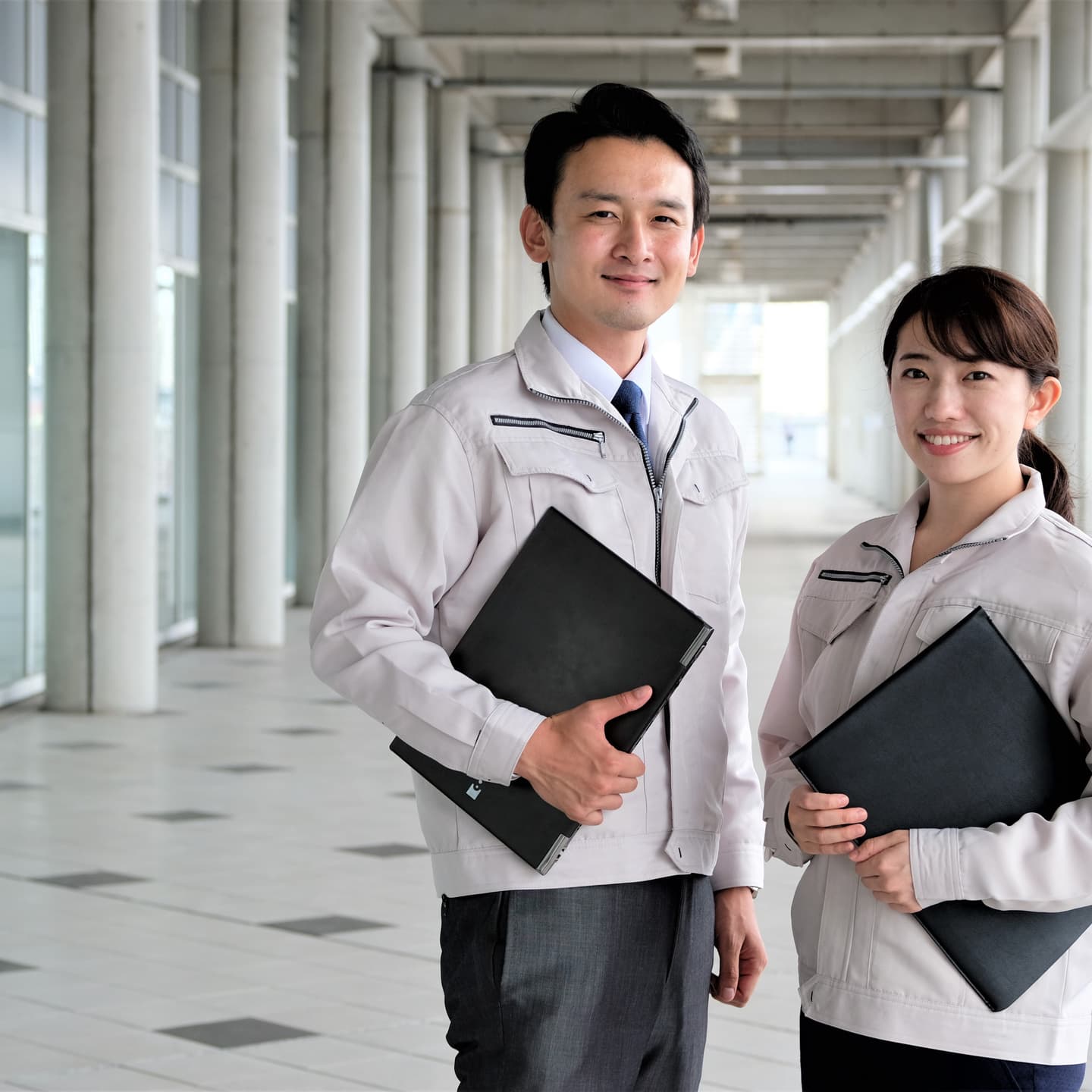 企業ビジネス英語研修を受けることで、職場でのコミュニケーション能力を高めることができます。廊下でファイルを持った2人の専門家が話し合っている様子。
