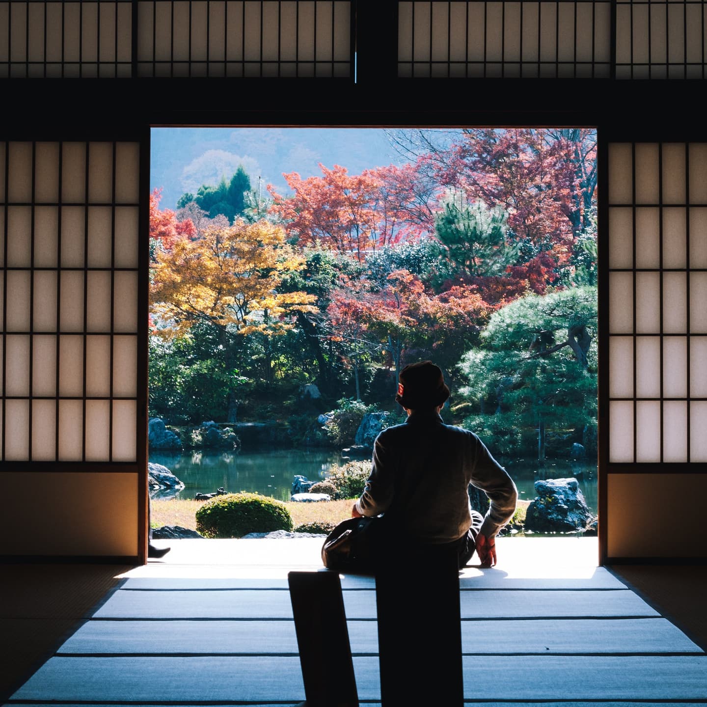 企業日本語研修を受けた外国人従業員が、和室の畳に座りながら秋の紅葉が美しい日本の庭園を眺めて心を落ち着かせている様子。